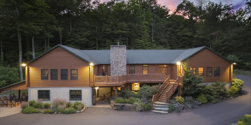 A spacious wooden lodge with a stone chimney, lit at dusk