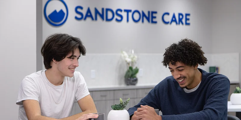 Two young men laughing at a table in a rehab center.
