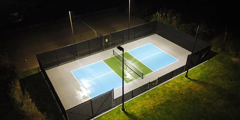 A lit-up pickleball court at night with surrounding greenery.