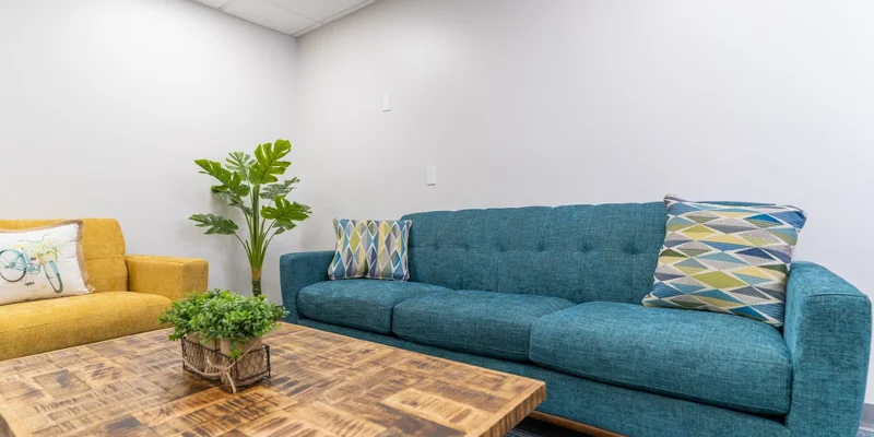 Cozy lounge with a blue couch, yellow armchair, and wooden coffee table.