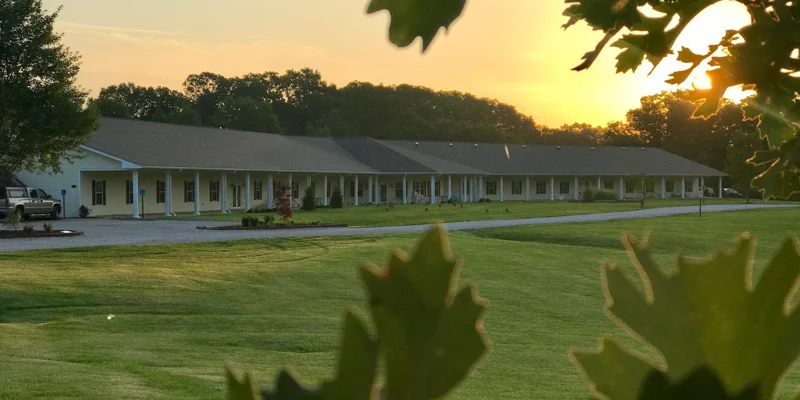 A rehab facility at sunset with a large lawn and wrap-around porch.