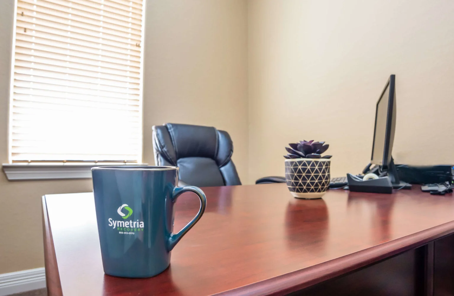 A professional office desk with a Symetria Recovery coffee mug.