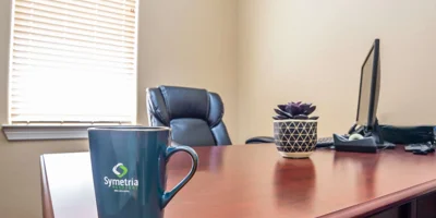 A professional office desk with a Symetria Recovery coffee mug.