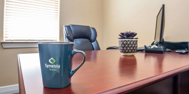 A professional office desk with a Symetria Recovery coffee mug.