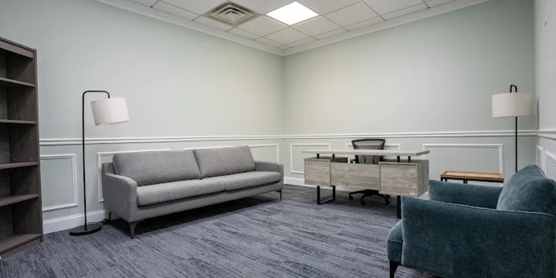 Office space with a gray couch, desk, and bookshelf.