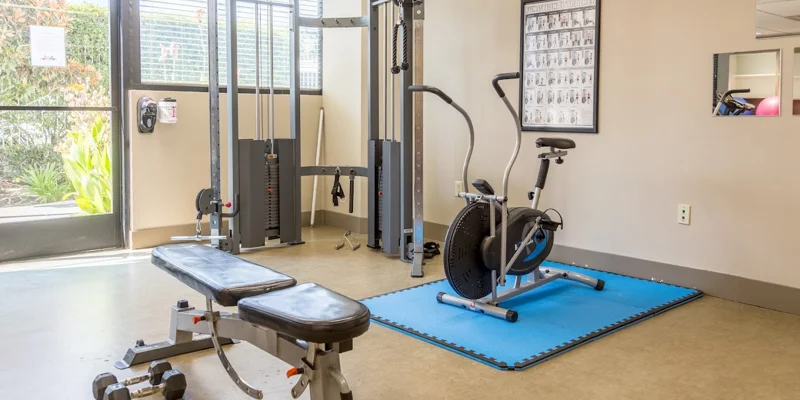 A small gym with exercise machines, a bench, and a training poster