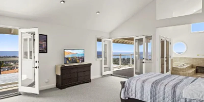 A bright bedroom with large windows, a bed, and a view of the ocean.