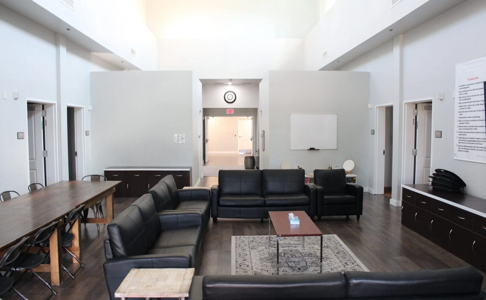 Common area with black couches, dining table and a whiteboard,.