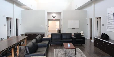 Common area with black couches, dining table and a whiteboard,.