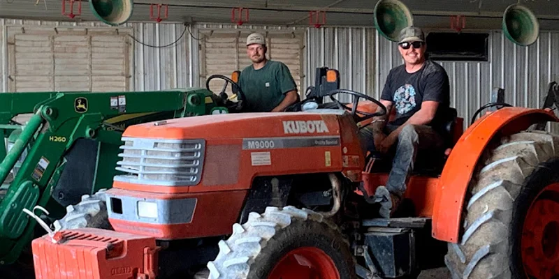 Smiling man on a tractor indoors with another person in the background.