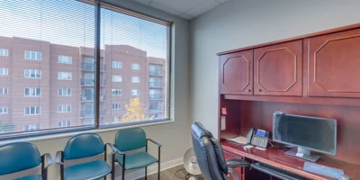 A small office with a desk, chairs, and a large window.