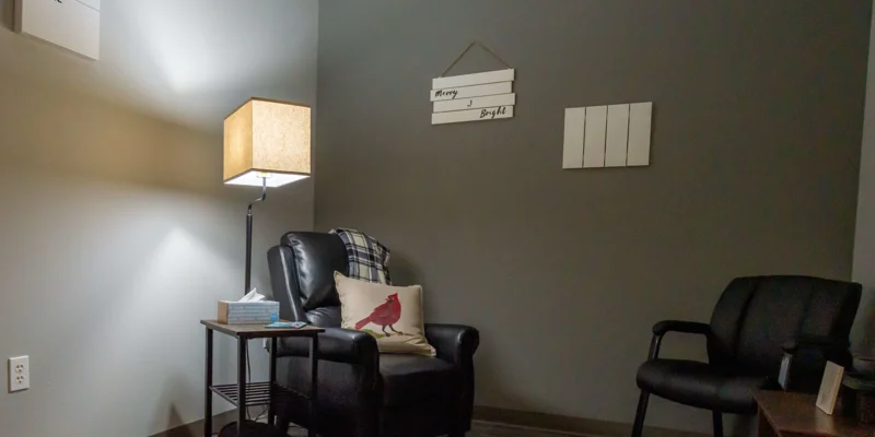 A cozy counseling room with a leather chair, lamp, and wall decor.