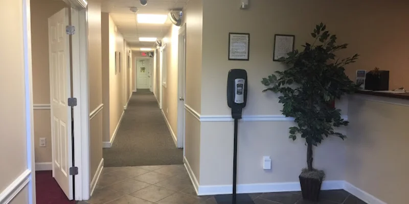 A hallway in a rehab facility with beige walls and a hand sanitizer station.