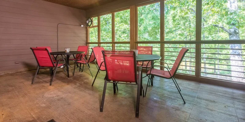 Screened porch with red chairs and a forest view