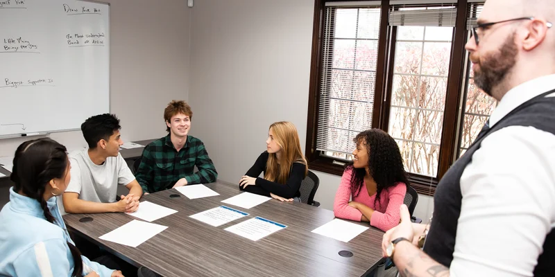 Young adults sitting at a table with a facilitator standing.