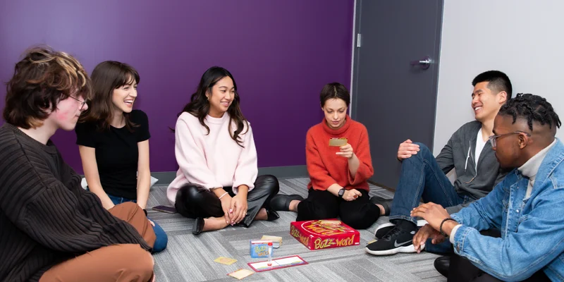 Group of young adults sitting on the floor playing a board game.
