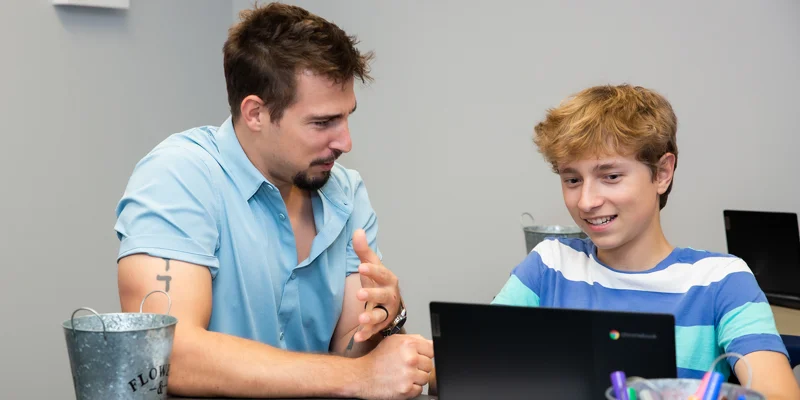 Adult helping teen with laptop during a therapy session.