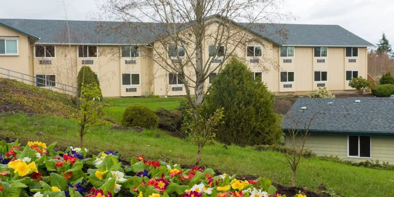 Facility exterior sits behind a garden and a smaller building.