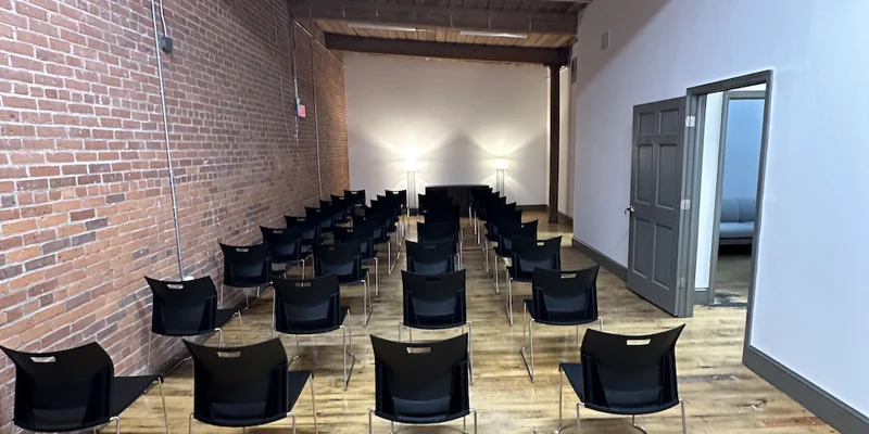 Lecture-style room with rows of black chairs and exposed brick walls