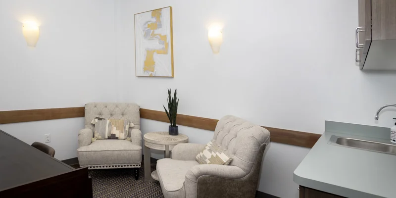 Small office space with two beige chairs, a sink, and abstract wall art.