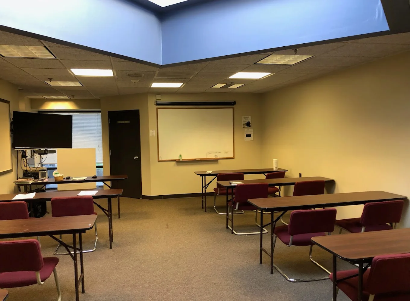 Classroom with chairs and tables behind a whiteboard, a TV, and a skylight above.