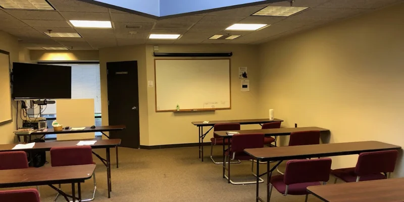 Classroom with chairs and tables behind a whiteboard, a TV, and a skylight above.