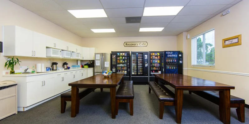 Cafeteria with wooden tables, vending machines, and kitchen area.