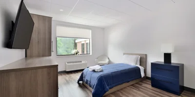 A clean bedroom with a blue comforter and TV.