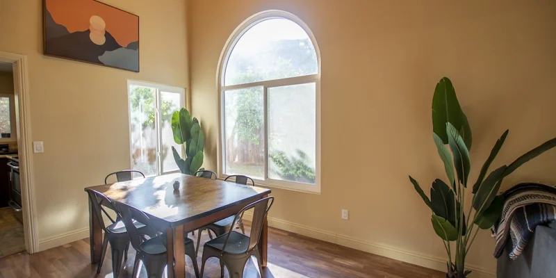 A dining area with a large arched window and green plants.