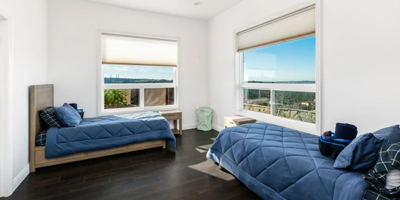 Shared bedroom with two beds and large windows.