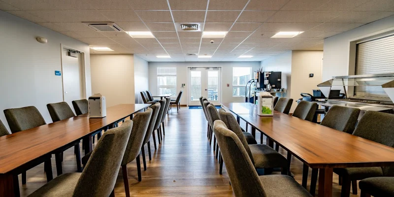 Dining area with long wooden tables and upholstered chairs.
