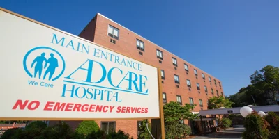 The entrance of AdCare Hospital with a sign and red brick exterior.