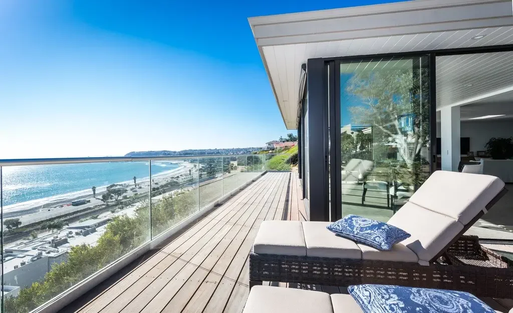 Ocean-view balcony with lounge chairs and glass railing.