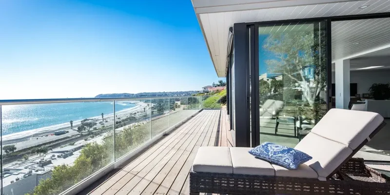 Ocean-view balcony with lounge chairs and glass railing.