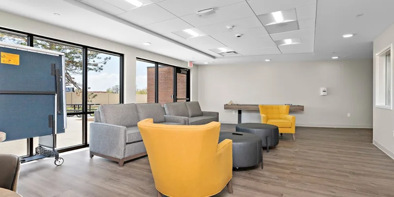 A recreation room with yellow chairs, a ping pong table, and sofas.
