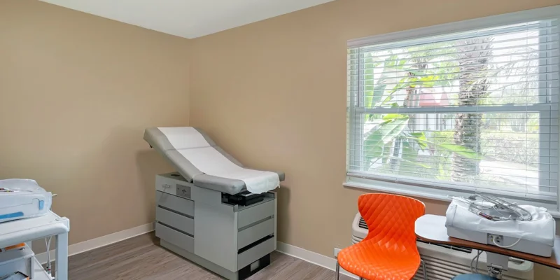 A medical examination room eith exam table, and chair.