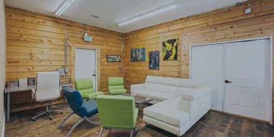 Wooden-walled lounge with white sofas and green chairs.