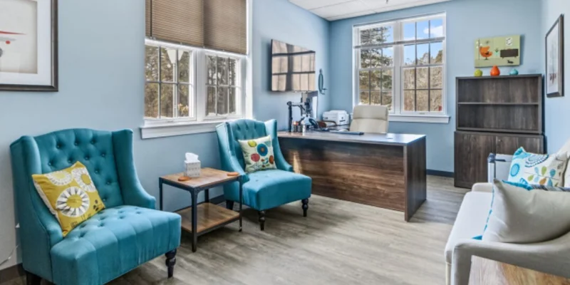 Therapy room with chairs, a desk, and windows.
