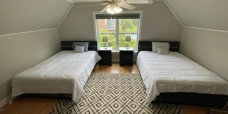 A bedroom with two beds, a ceiling fan, and a window view