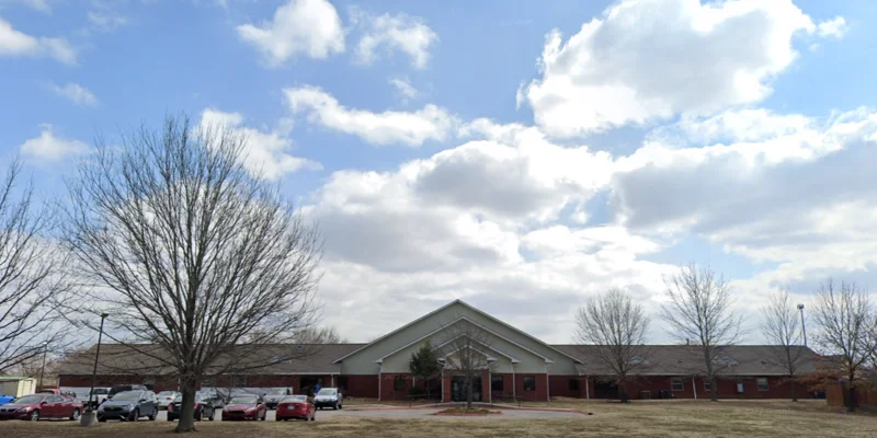 Front of facility featuring trees and parking by entrance.