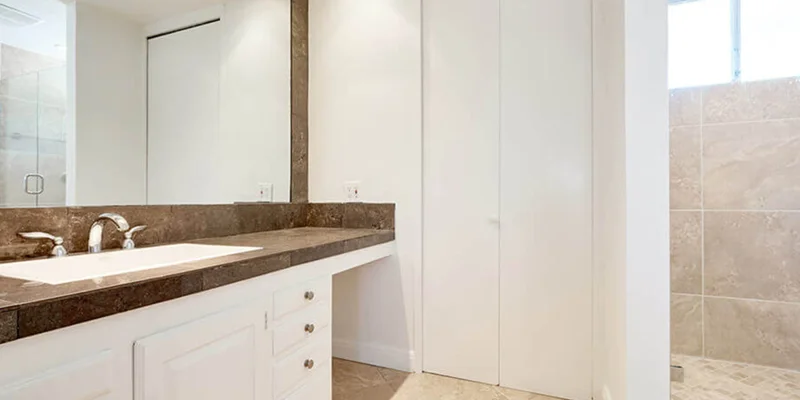 A bright bathroom with a large mirror, white cabinets, and a tiled shower.