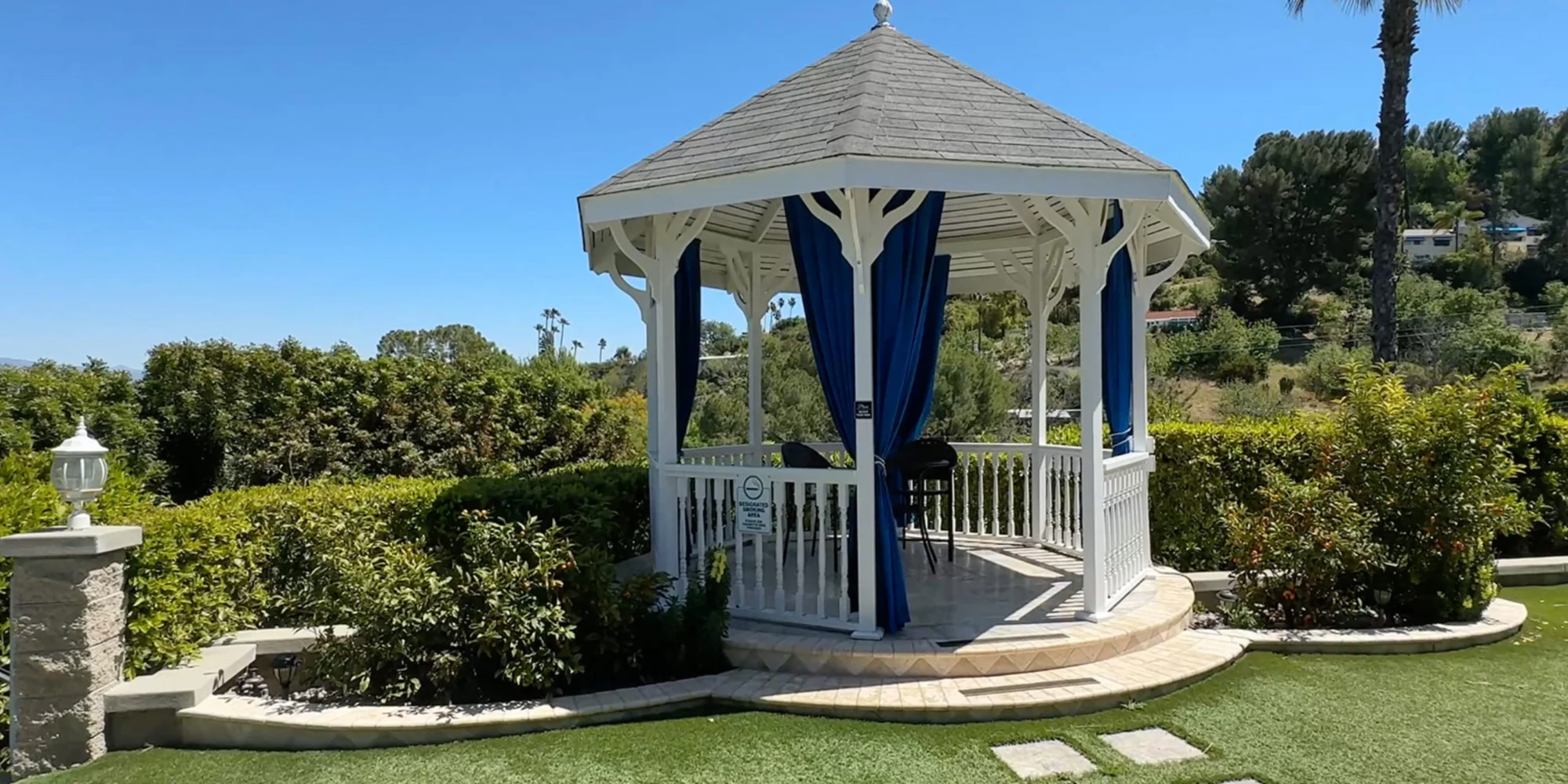 A white gazebo with blue curtains overlooking green hills.