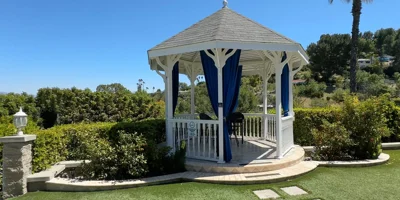 A white gazebo with blue curtains overlooking green hills.