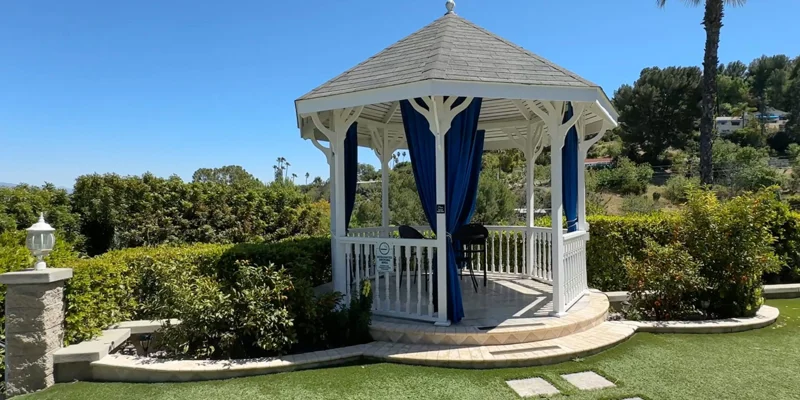 A white gazebo with blue curtains overlooking green hills.