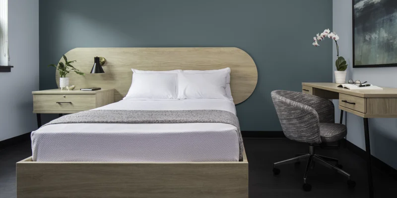 Bed with wood frame, teal wall, desk, and chair