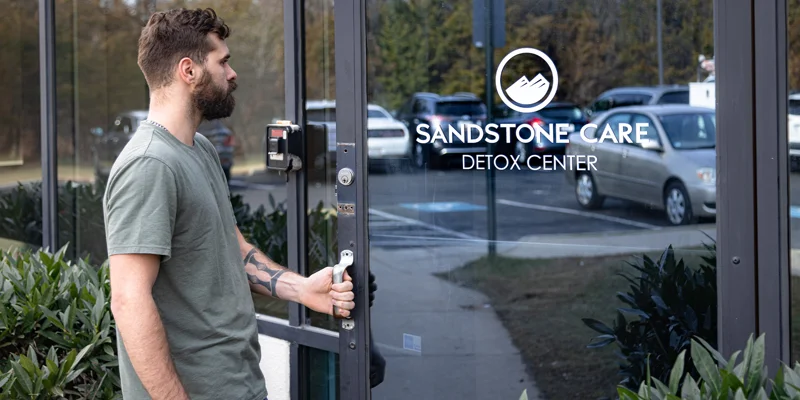 Man opening the glass door of a Sandstone Care detox center.