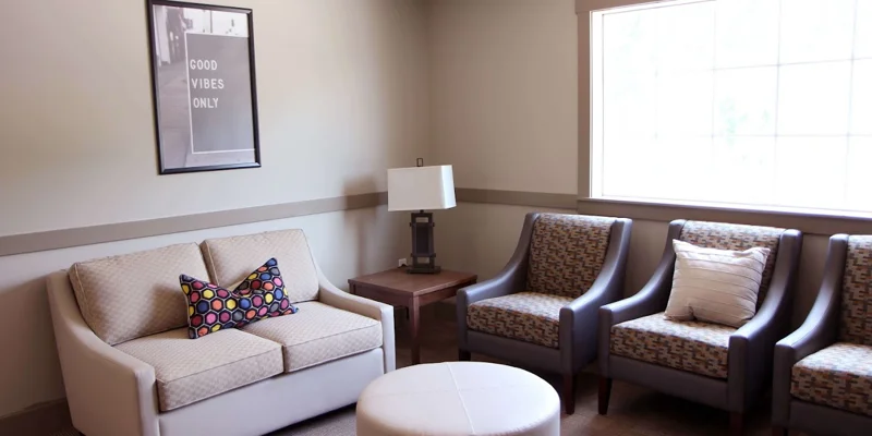 Cozy waiting room with a beige couch, gray chairs, and a "Good Vibes" sign.
