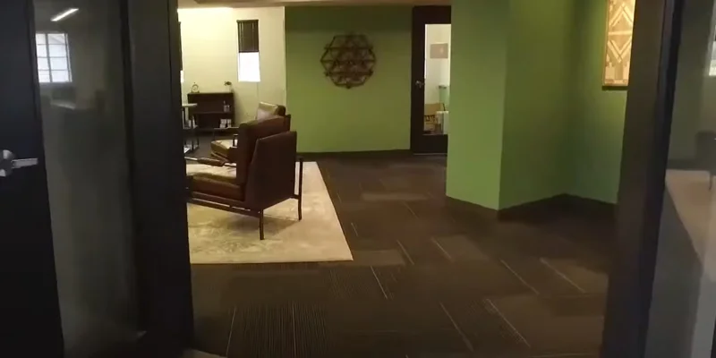 A hallway with green walls leading to a seating area with leather chairs