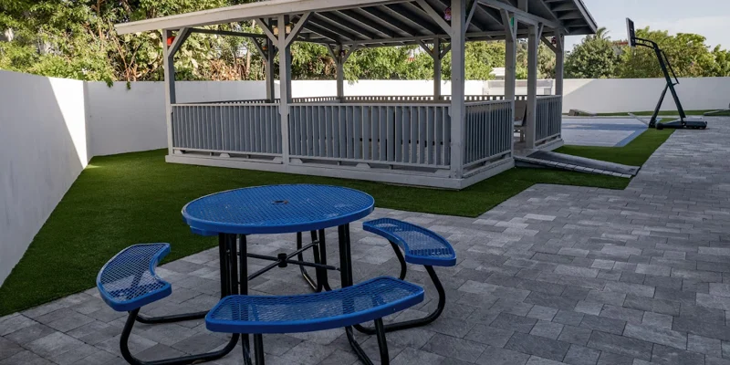 Outdoor area with a gazebo, table, and a basketball court.