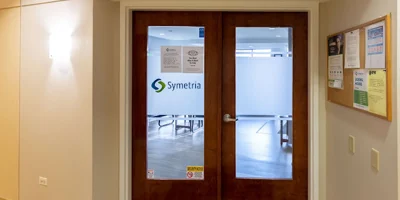 Glass double doors with a "Symetria" logo leading to a facility.